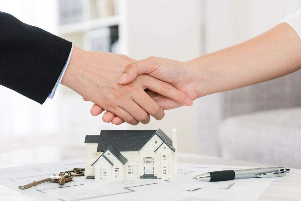 A man and woman shaking hands over a house.